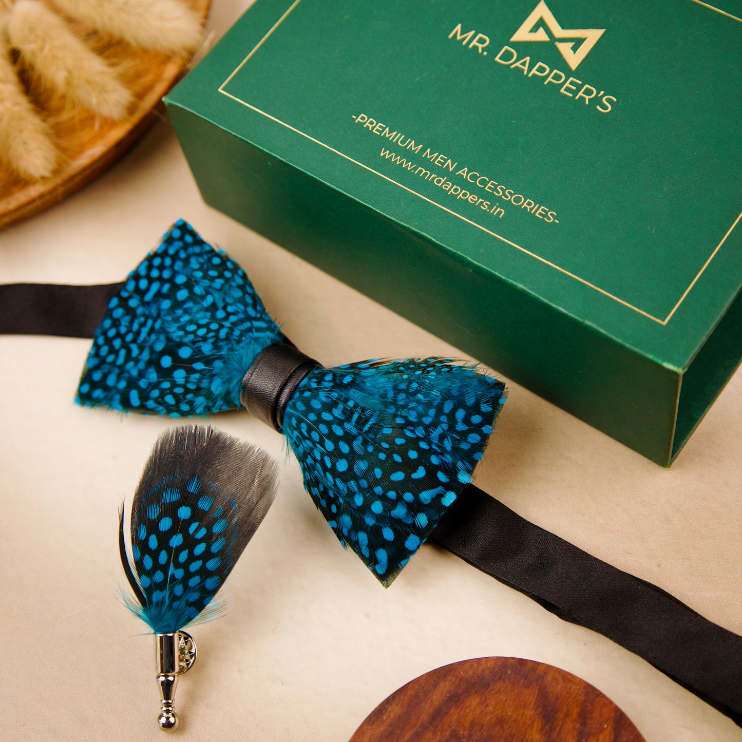 A blue and black feather bow tie and pin set next to a green box labeled "Mr. Dapper's.