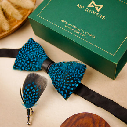 A blue and black feather bow tie and pin set next to a green box labeled "Mr. Dapper's.