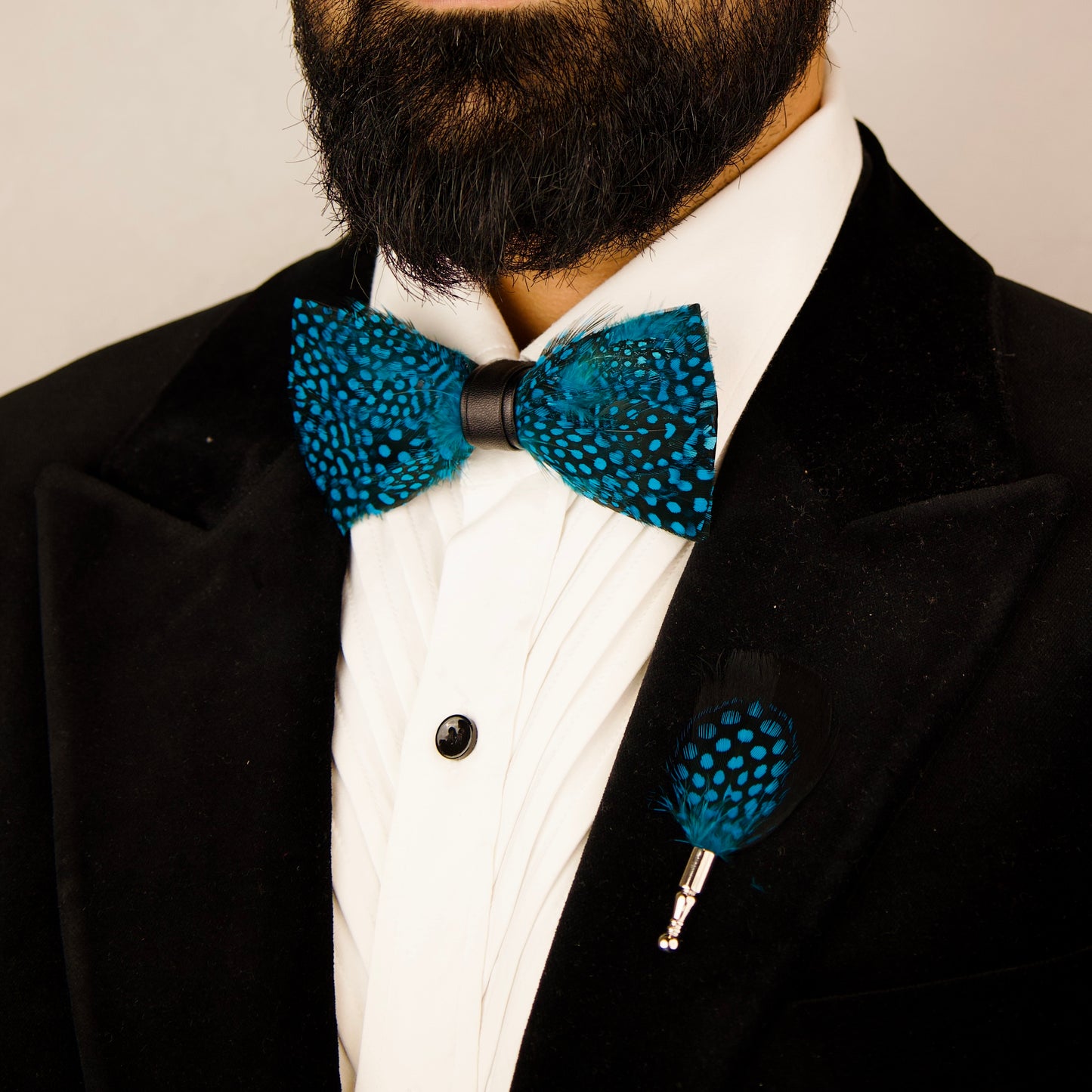 A blue and black feather bow tie and pin set next to a green box labeled "Mr. Dapper's.