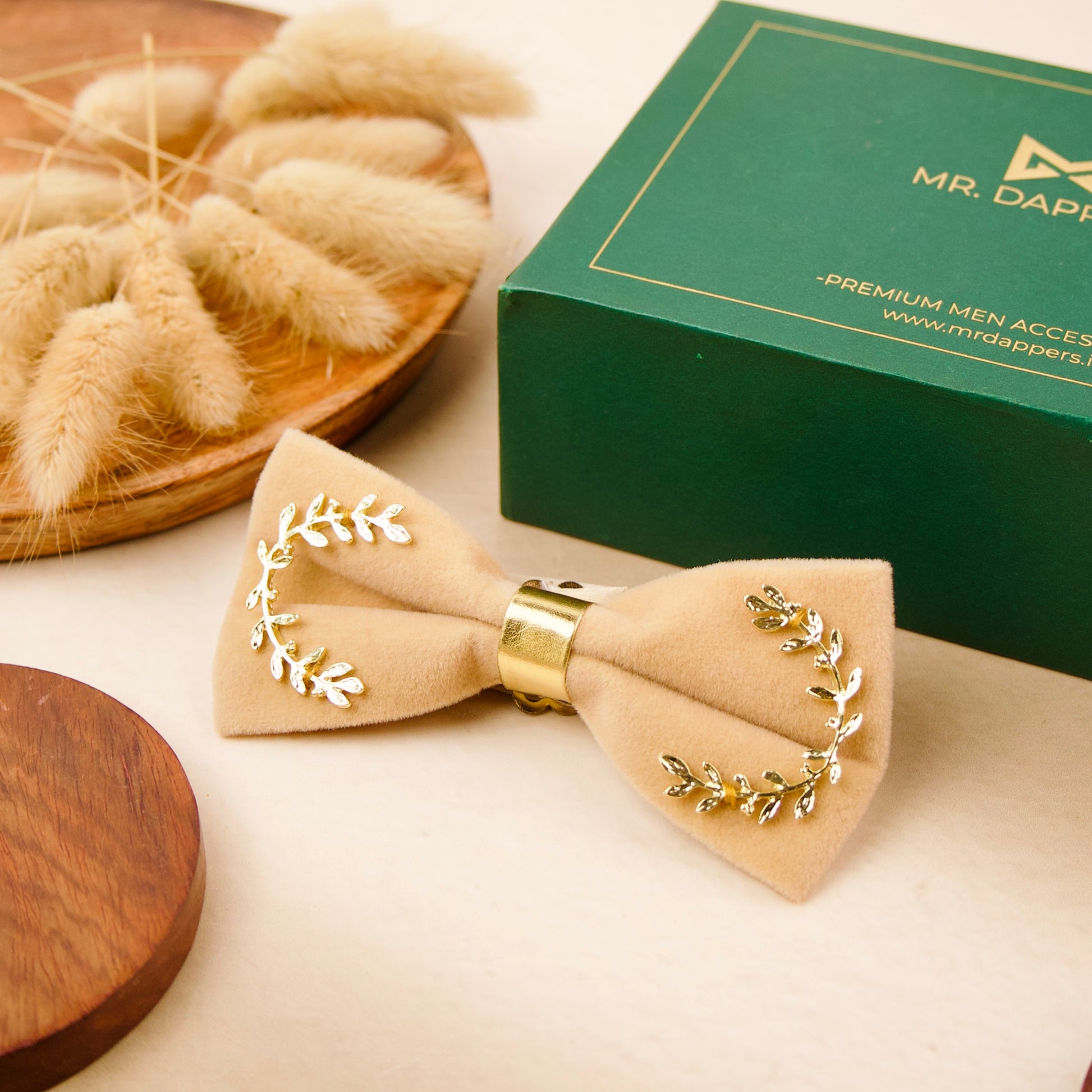 A bow tie adorned with gold leaves, elegantly displayed in a green box.