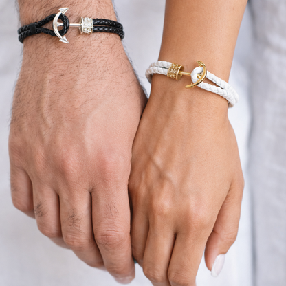 Two hands wearing anchor-themed bracelets on a plain background
