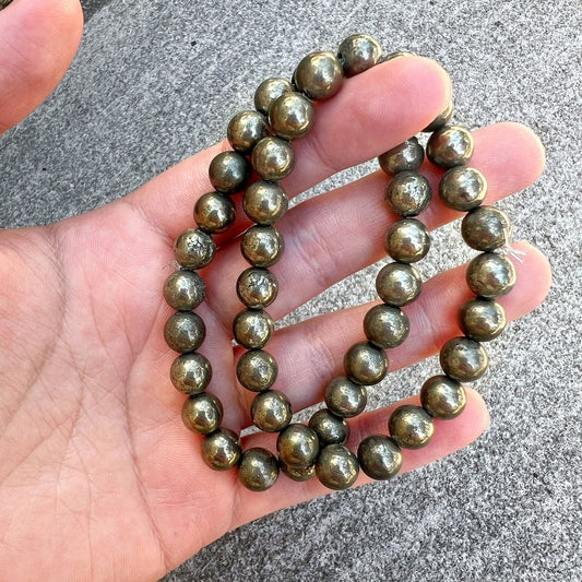 Hand holding a string of metallic beads on a concrete surface