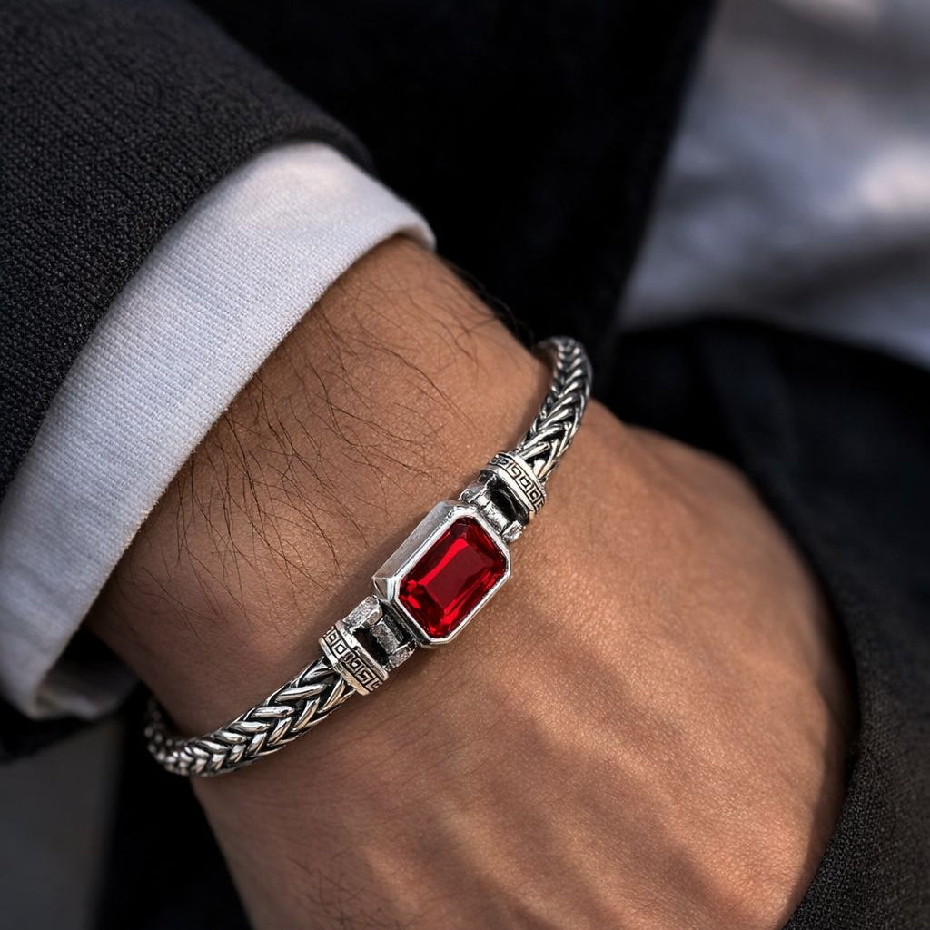 Bracelet with a red gemstone on a wrist, wearing a dark suit and white shirt.