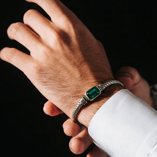 Hand wearing a silver bracelet with a green gemstone on a black background